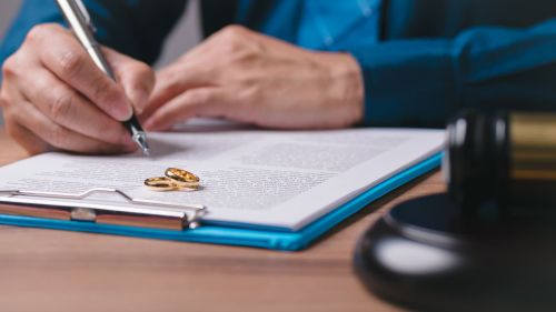 A man is writing on a piece of paper with a pen. The paper has a ring on it