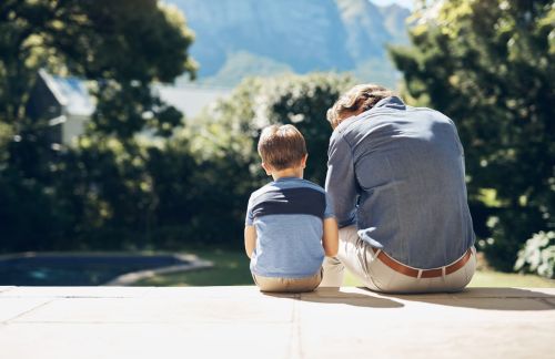 Father sitting and comforting sad son with autism, mental disorder and depression on garden step backyard patio. Back view of caring, loving and kind single parent supporting, comforting and talking